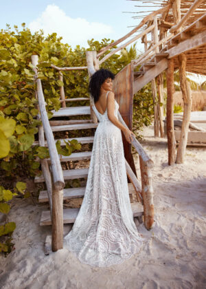 Eine Frau steht vor einer Strandtreppe im romantischen Brautkleid von Herve Paris aus der Babs Kollektion.
