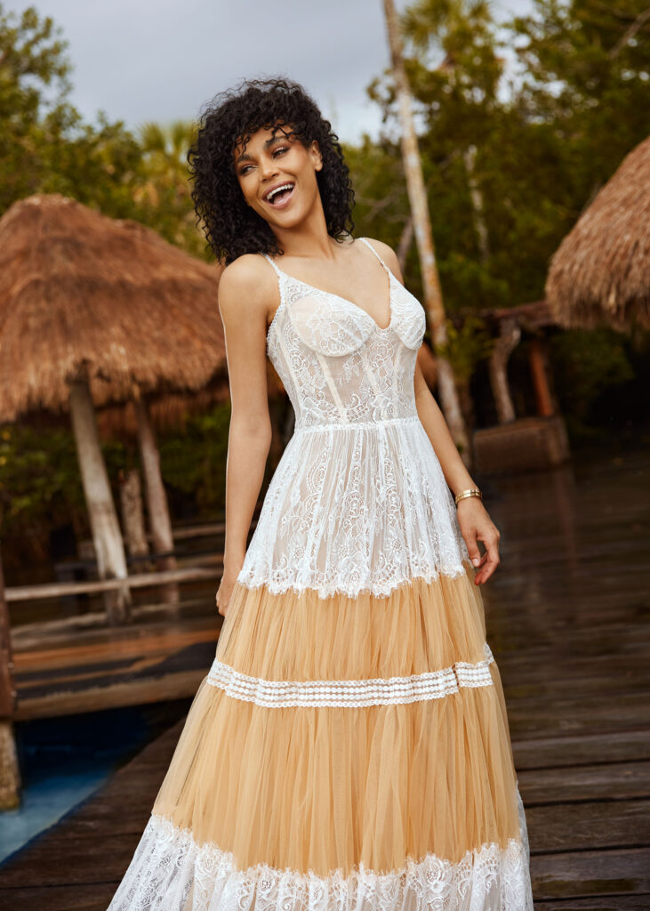 Lachende Frau auf einem Steg im Meer und trägt dabei ein Hochzeitskleid von Herve Paris aus der Betina Kollektion