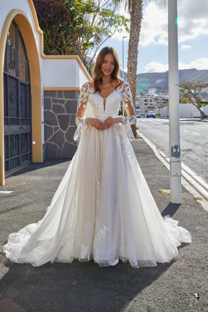 Eine Frau steht vor einer Mauer im Hochzeitskleid von Euro Mode aus der Novabella Kollektion.