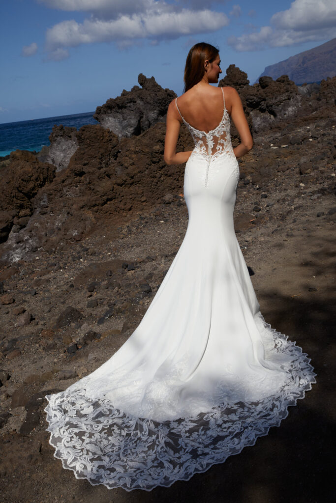 Braut steht auf den Klippen und schaut auf das Meer während sie ein Brautkleid von Euro Mode trägt.